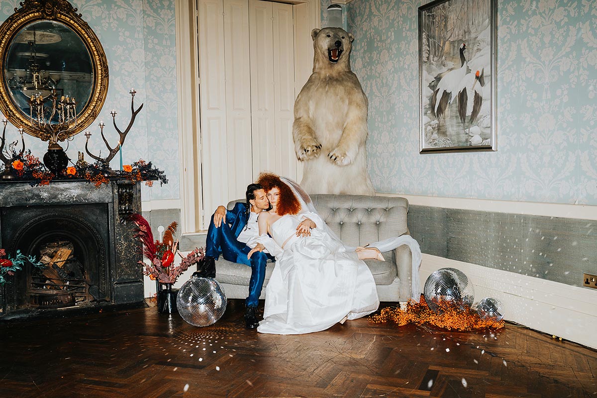 maximalist wedding couple lounging on a couch in an extravagant interior featuring a taxidermy polar bear