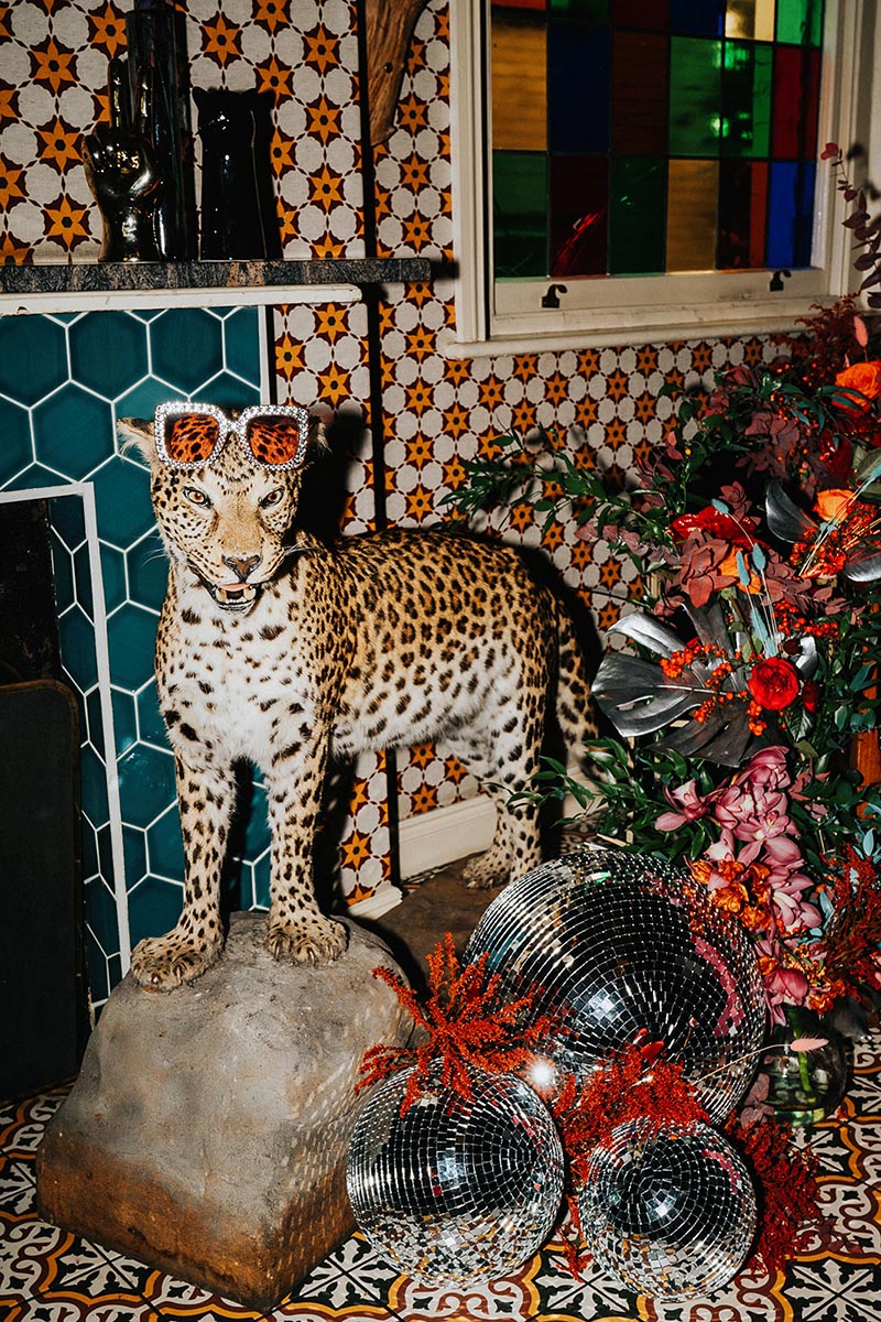 a stuffed leopard with sparkly sunglasses on its head surrounded by flowers and disco balls as decor for a maximalist wedding