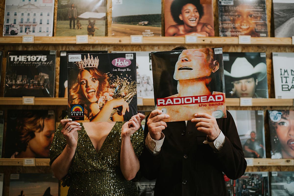 A couple hold albums in front of their faces in a record shop in Brighton on their wedding day