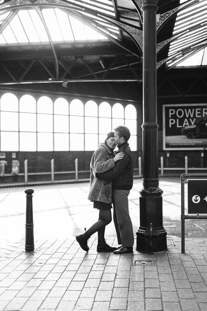 A couple pose for cinematic engagement photography at Brighton train station