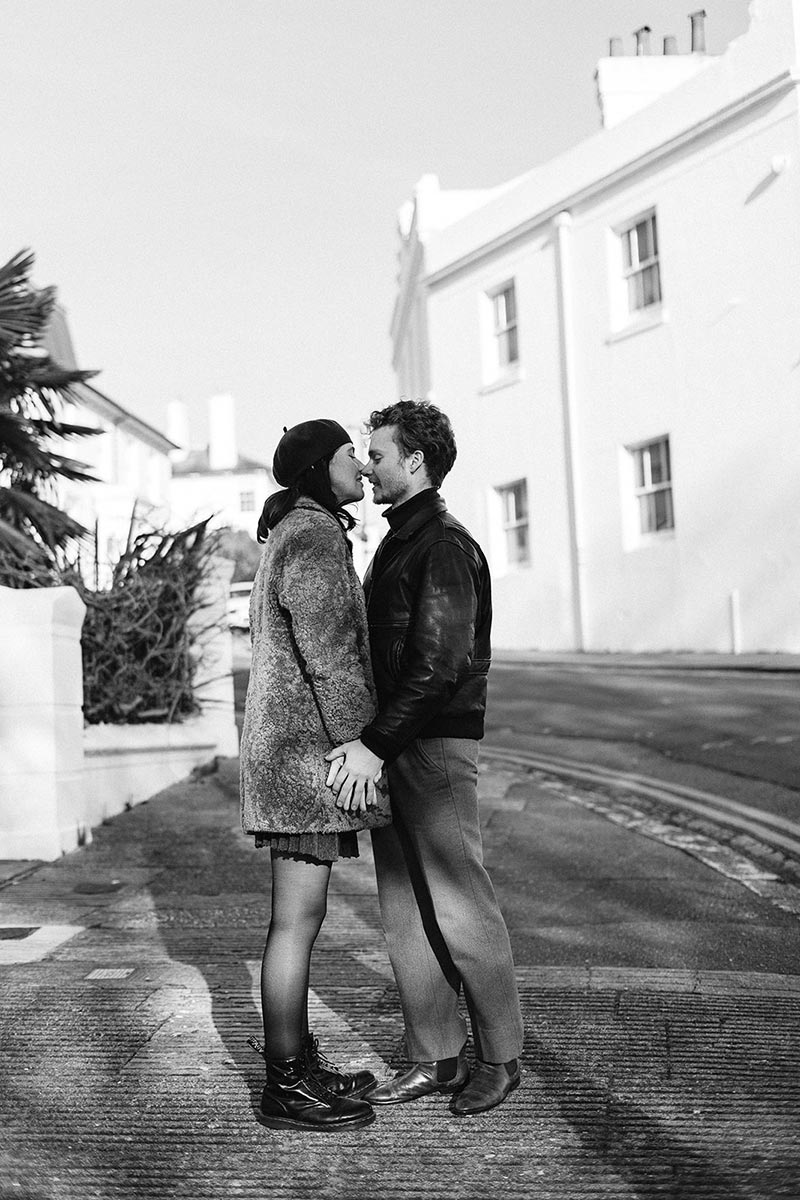 A couple stand facing each other and holding hands, looking into each others' eyes for a cinematic engagement photo in a street in Brighton