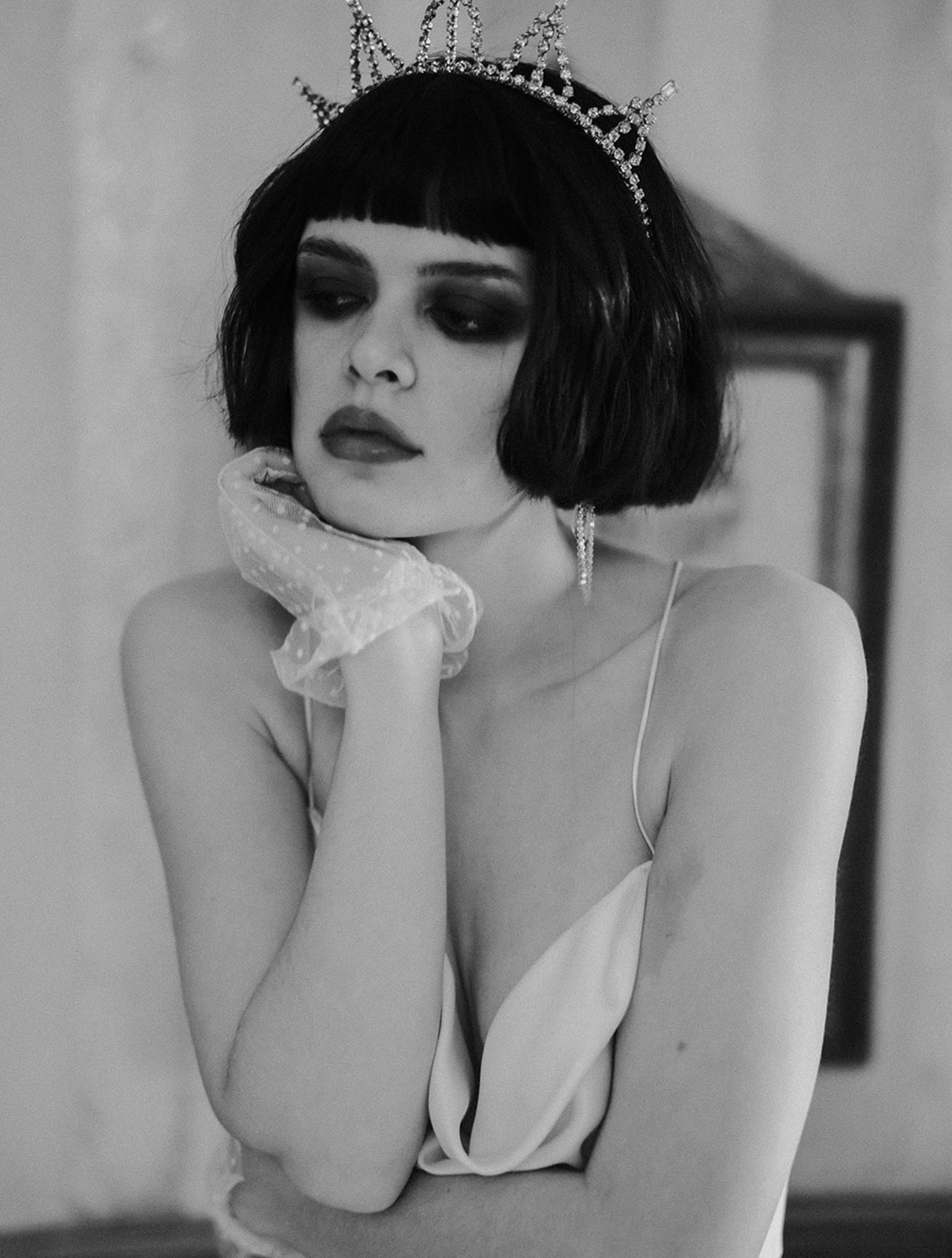 A female model with short hair sits on a chair looking off camera wearing white trousers and a beaded bra top by Brighton Wedding Photographer