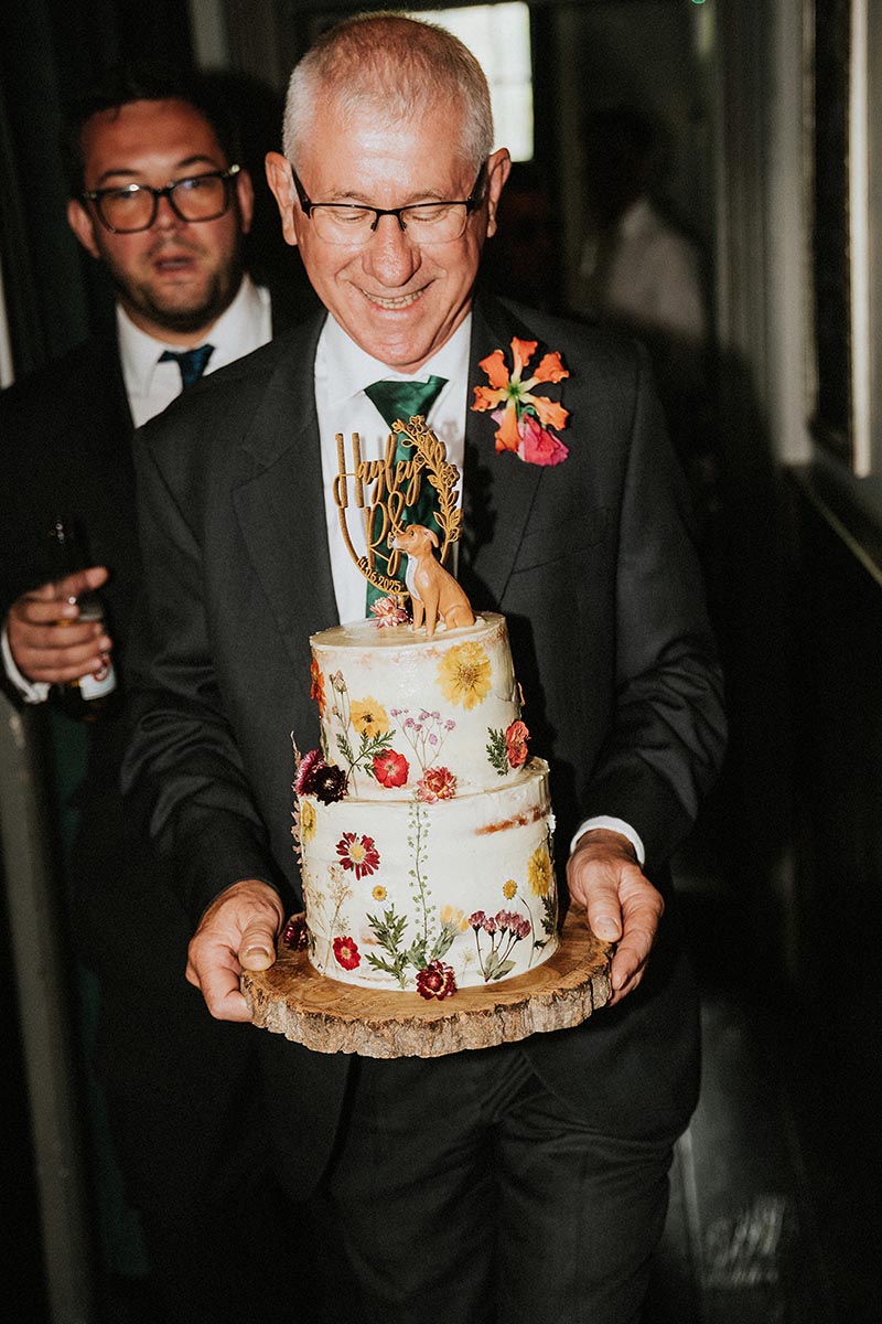 Bride's dad carries the wedding cake at the reception at The Joker Pub in Brighton