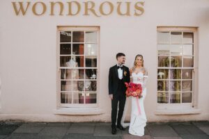 Couple pose outside a pink shop in Brighton before going to their reception at The Joker Pub
