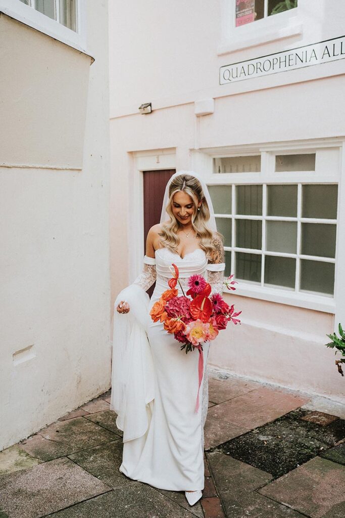 bride on her wedding day in brighton in front of a pink wall carrying a bright floral bouquet