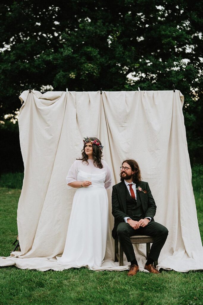 Couple pose in front of a photography backdrop in a field at the secret barn sussex on their wedding day