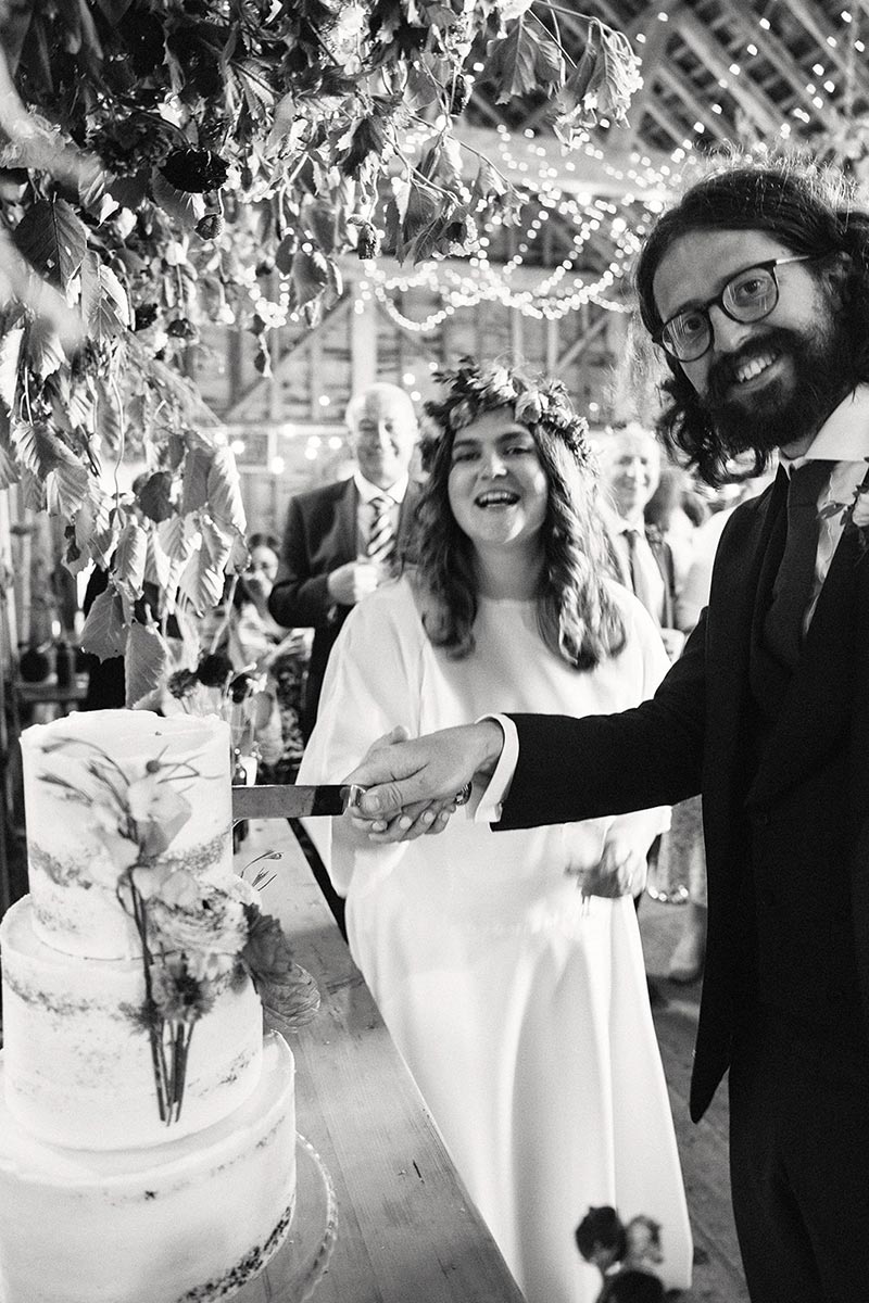 A wedding couple cut their cake in the rustic surroundings of the secret barn