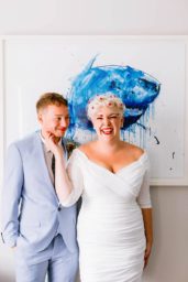 Couple at their artist residence hotel wedding in london. They are posing in one of the hotel bathrooms in front of a shark picture. The bride is holding the groom's face and laughing to camera.